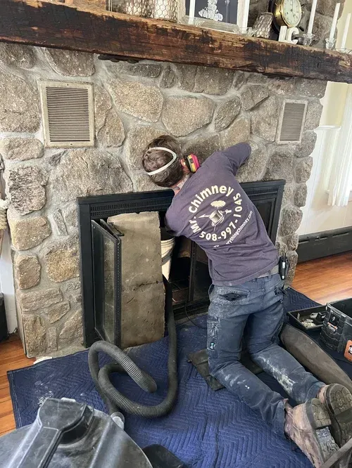 Technician performing a chimney sweep, removing soot with a rotating brush