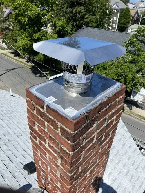 Close-up of a stainless steel chimney cap installed on a chimney crown
