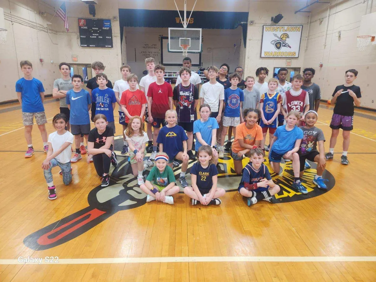 A friendly camp administrator at a modern reception desk, surrounded by colorful camp posters and registration forms. The office is bright and welcoming, with natural light and cheerful decor, suggesting approachability and professionalism.