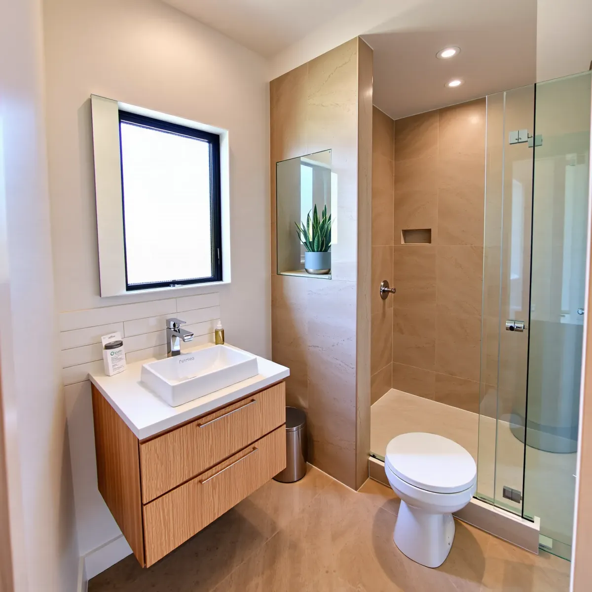 Modern small bathroom in Palms, CA with white subway tiles, floating oak vanity, glass shower, and natural light.