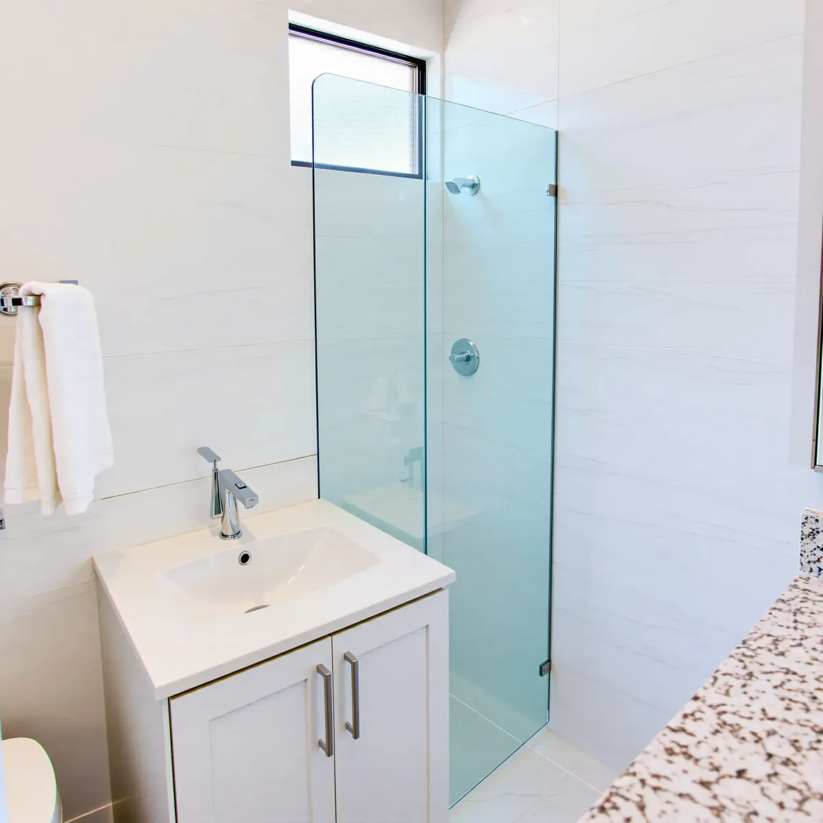 Remodeled small Hawthorne bathroom with glass shower, floating marble vanity, backlit mirror, gray tiles, and natural light.