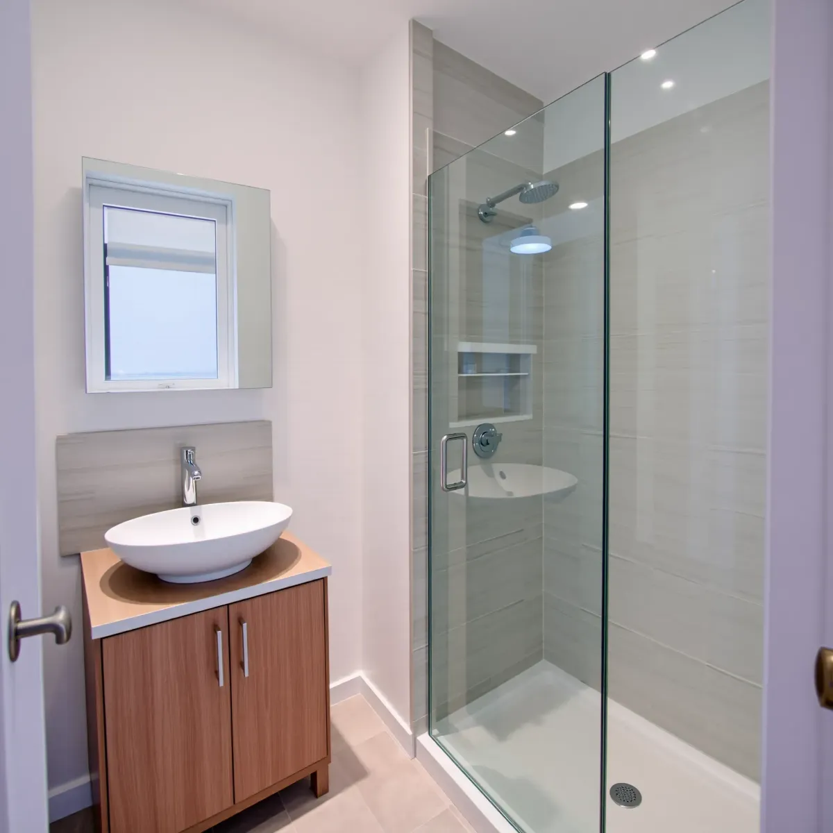 Modern Windsor Hills bathroom with gray tiles, white vanity, glass shower, and natural light in a cozy home.