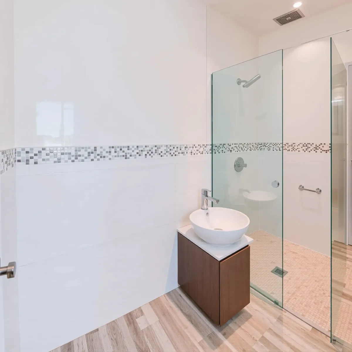 Small modern bathroom in Leimert Park, CA with white tiles, mosaic accents, vessel sink, glass shower, and warm lighting.