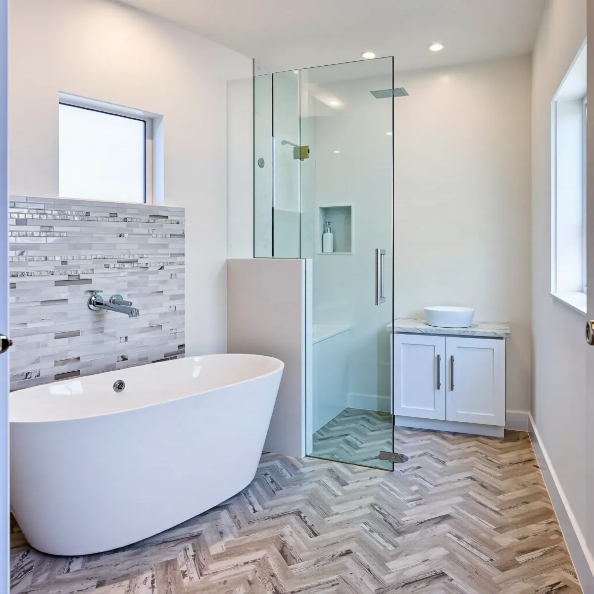 Modern renovated small bathroom in View Park, CA with a white bathtub, marble vanity, mosaic tiles, and frameless shower.