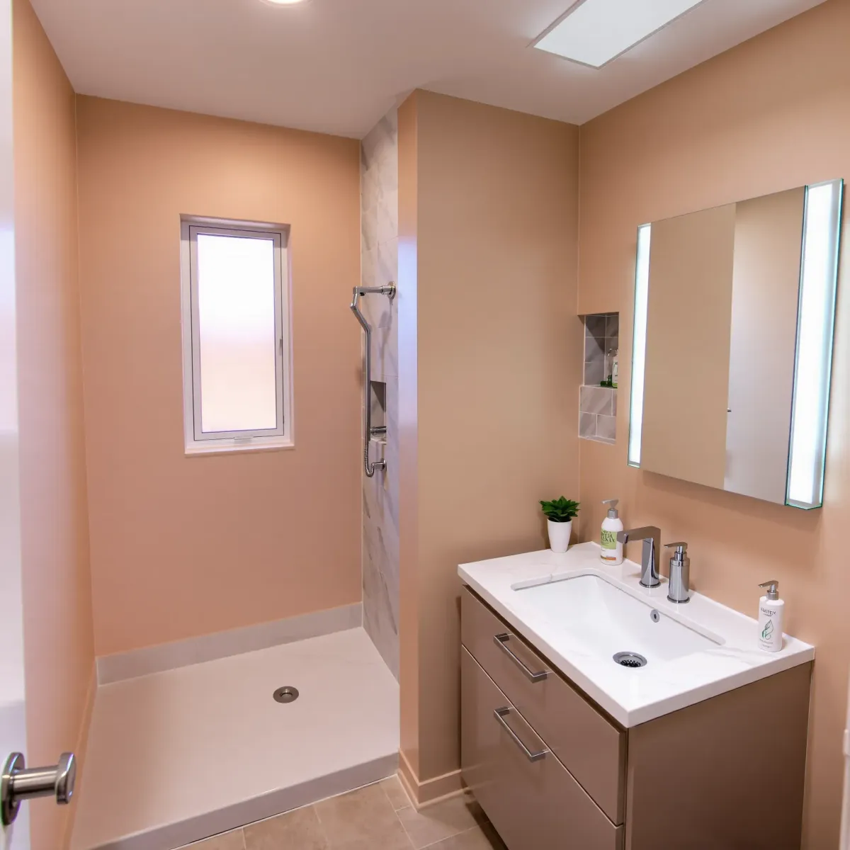 Small modern bathroom in Harvard Heights, CA with beige walls, white marble counters, glass shower, wall-mounted toilet, and upgraded fixtures.