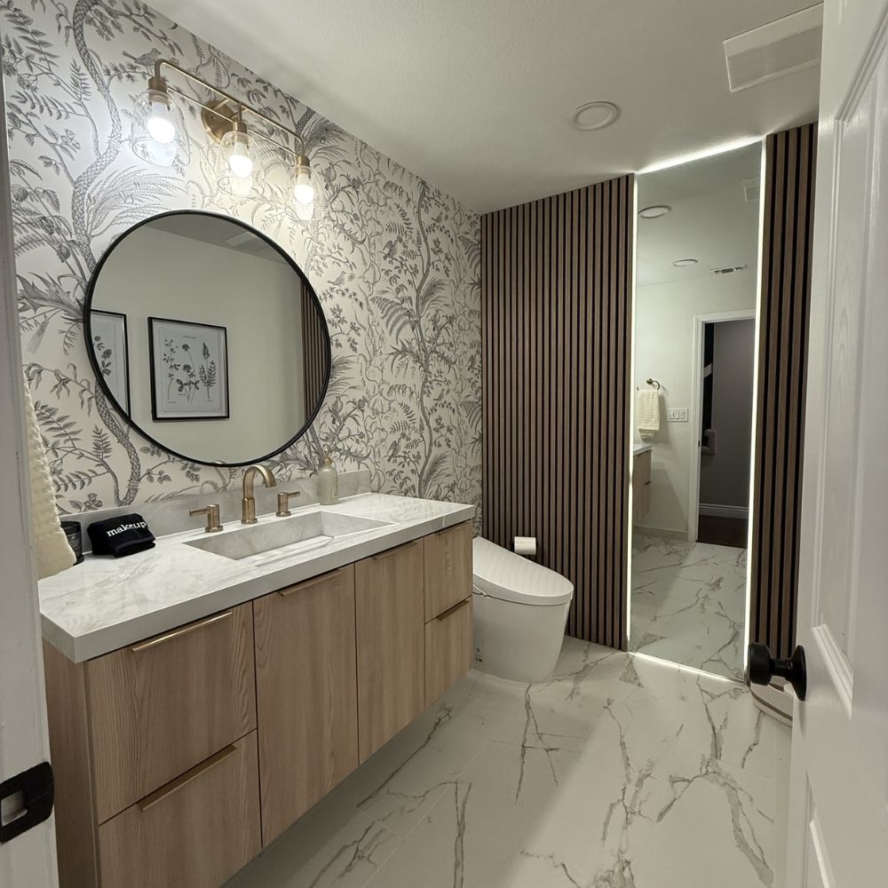 Modern vanity replacement with stone countertop, round mirror, and patterned wall finish