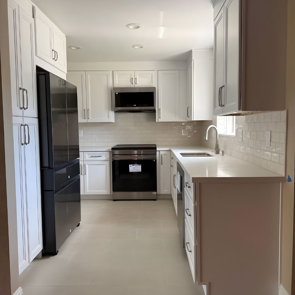 Compact modern kitchen renovation with white cabinets, integrated appliances, and clean tile flooring