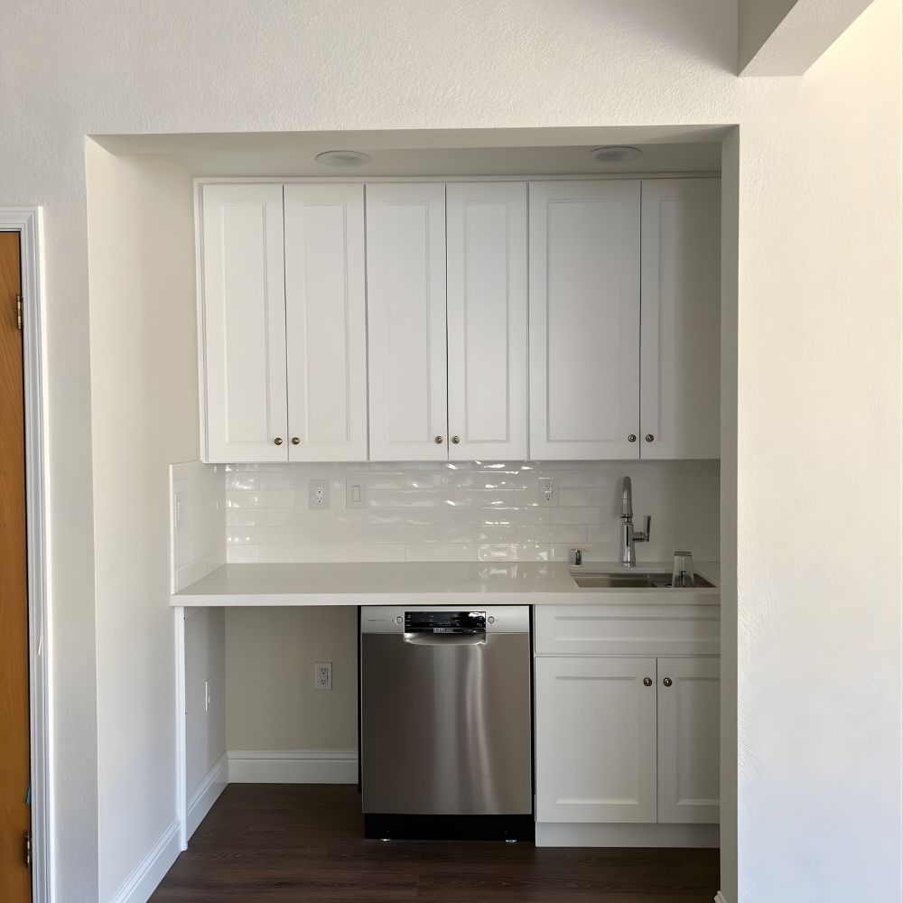 Built-in kitchenette with white cabinets, subway tile backsplash, and compact dishwasher