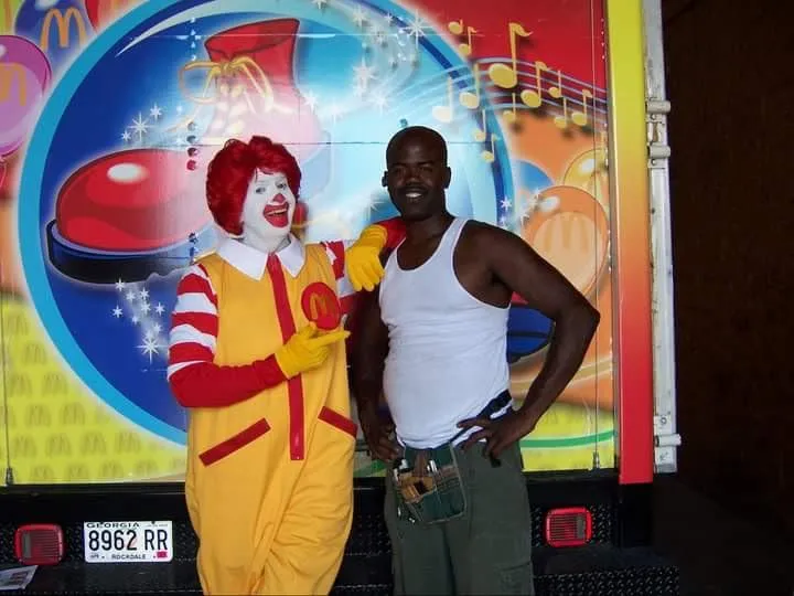 A diverse team of print professionals collaborating around a large-format printer, reviewing a freshly printed sign. The workspace is bright and organized, with vibrant signage samples on the walls. Everyone is focused and engaged, reflecting expertise and teamwork.