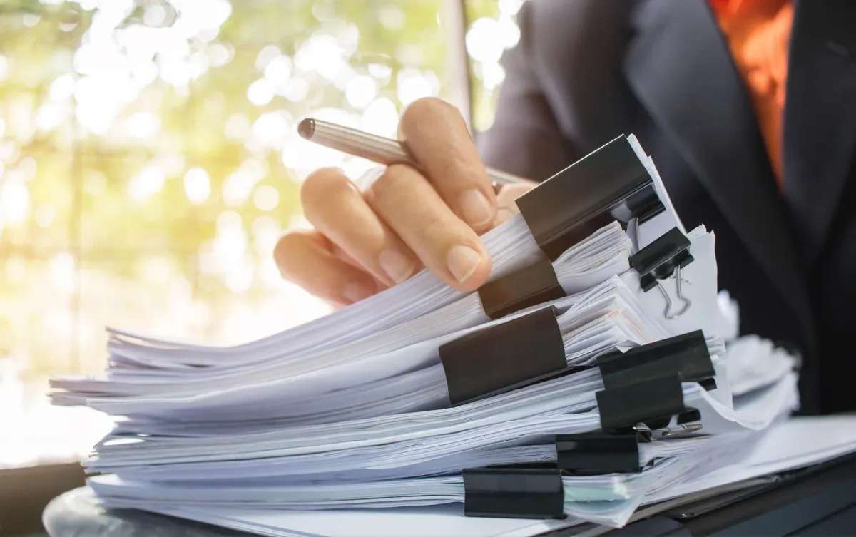 A person's hand holding a large stack of organized papers secured with binder clips