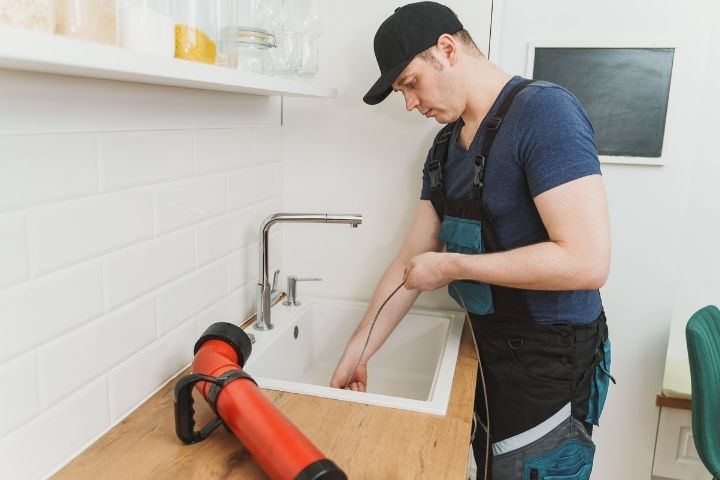 A plumber using a drain snake to clear a sink clog and resolve a drain backup.