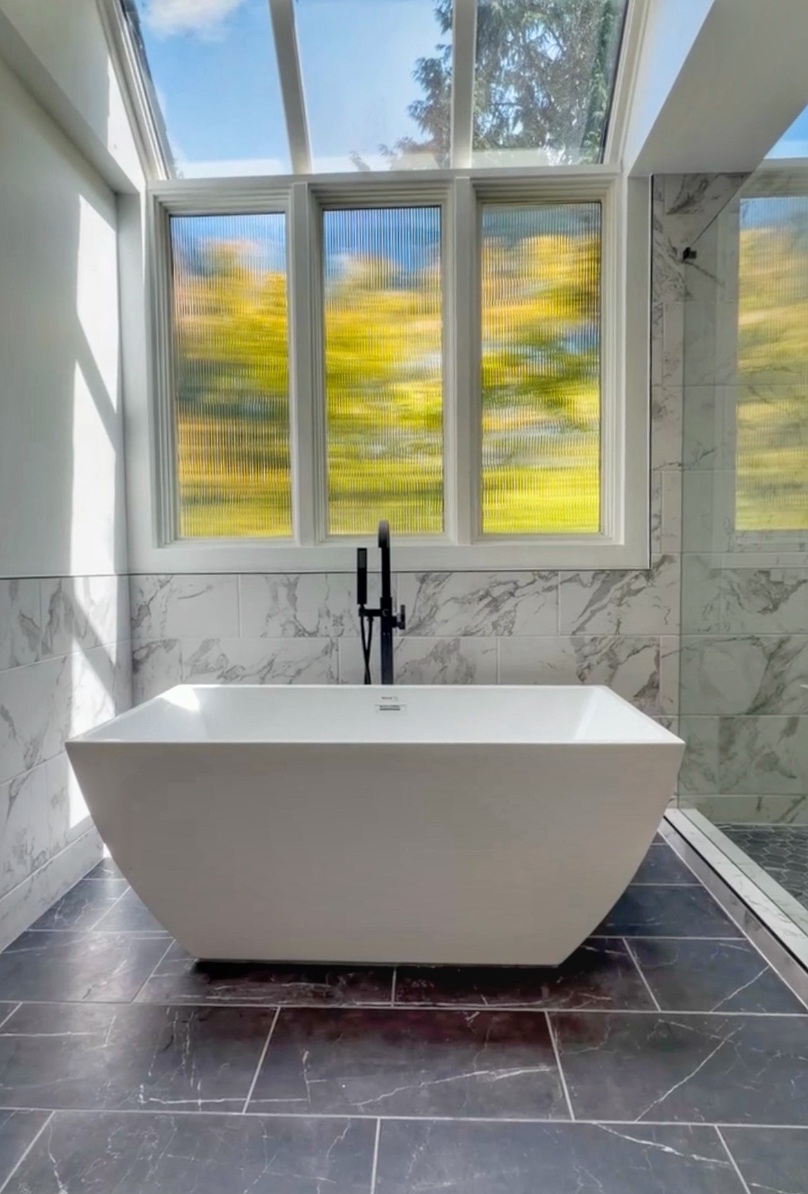 Maple Valley WA primary bathroom remodel featuring stand alone modern tub with new privacy glass next to tiled walk-in shower with glass enclosure.