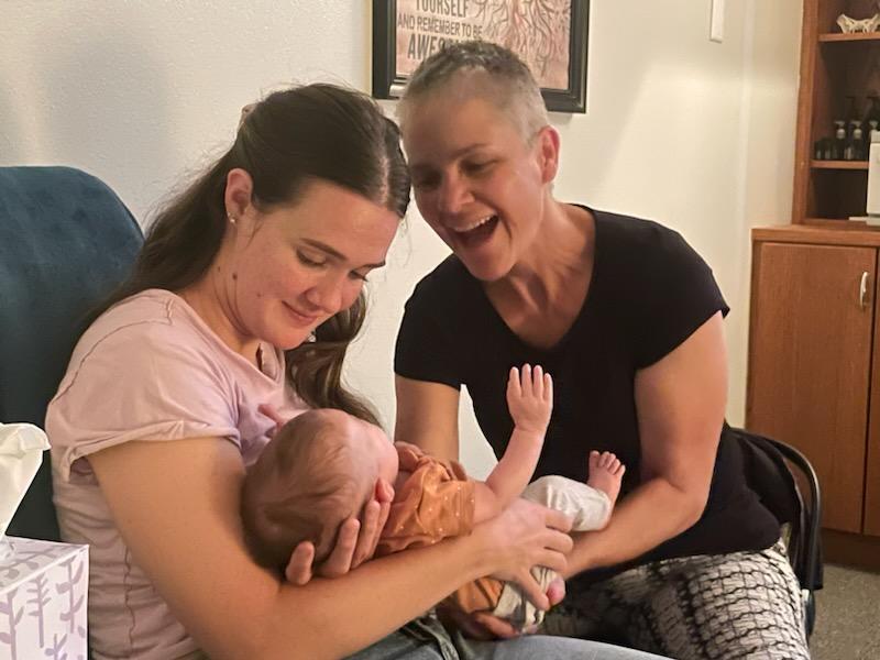 Karey Kosorok laughing with a mother holding her newborn during a pediatric CranioSacral Therapy session in St. George, Utah.