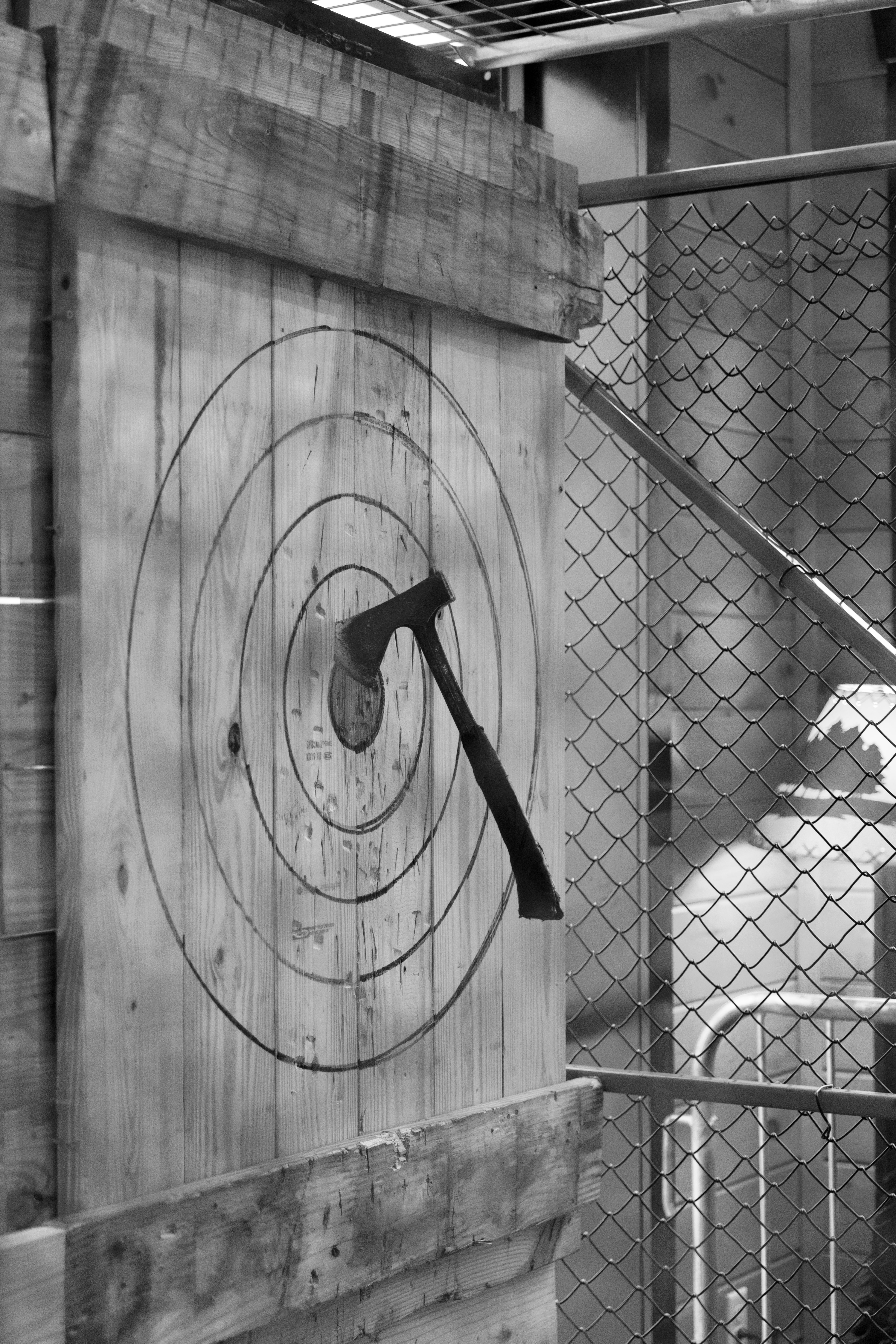 Axe embedded in a wooden target with concentric circles, showcasing a mobile axe throwing setup in a fenced area.