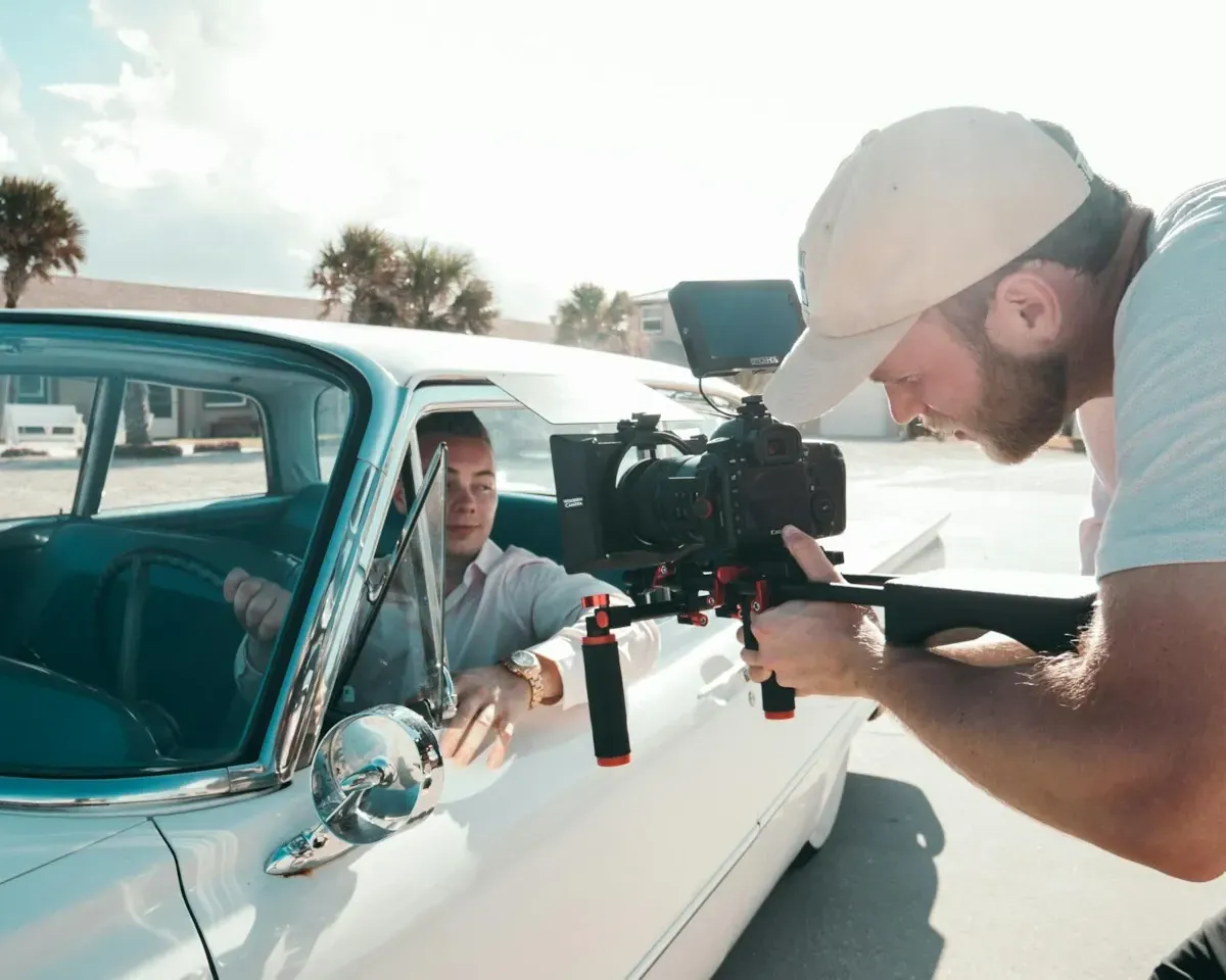 A photo of a videographer filming a young man in a classic car