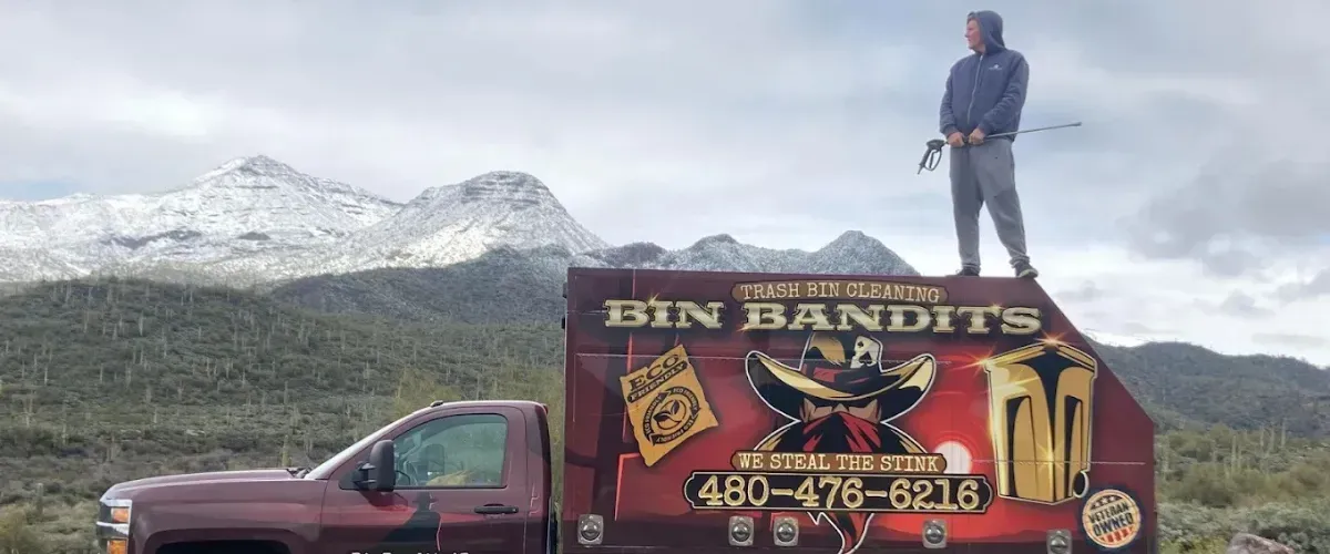 Bin Bandits team member standing on top of a custom truck holding a pressure washer with mountain views behind.