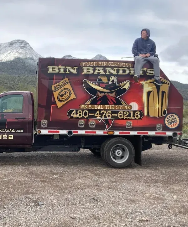  Side view of the Bin Bandits branded truck with a person sitting on top, set against a mountainous Arizona backdrop.