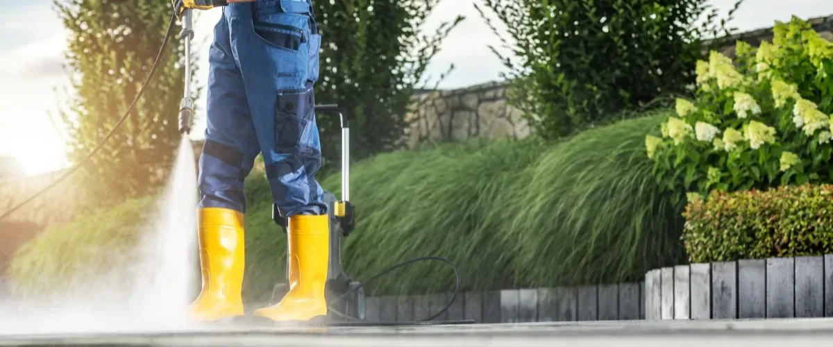 Professional performing driveway pressure washing wearing yellow boots