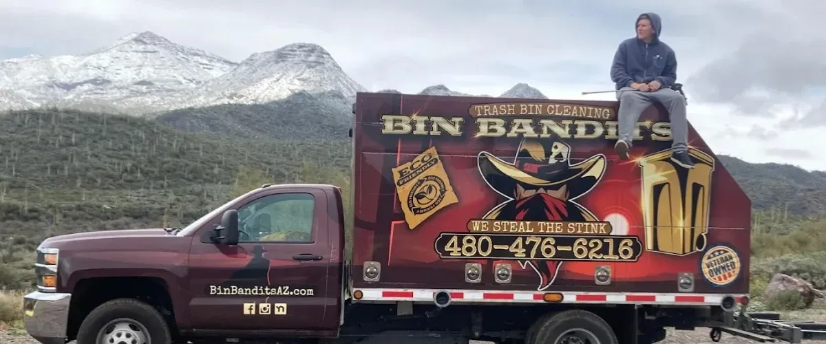 Bin Bandits trash bin cleaning truck parked in front of scenic Arizona mountains with a worker sitting on top.