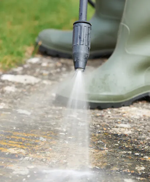 Close-up of a pressure washer nozzle spraying a concrete surface with rubber boots in view.