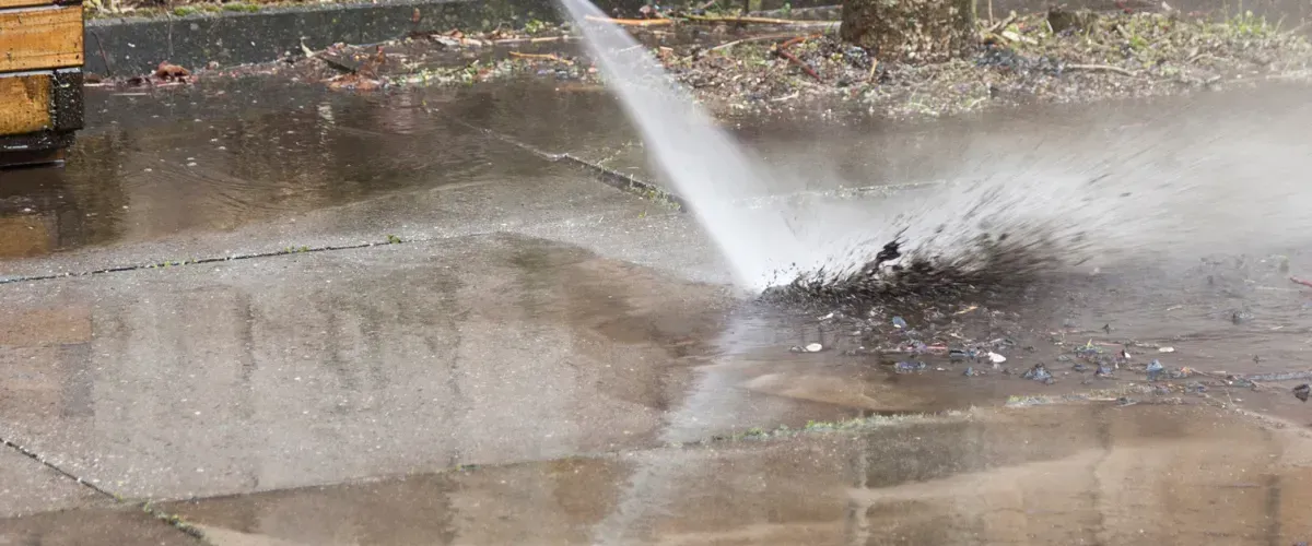 High-pressure water stream blasting mud and debris off a wet concrete surface.