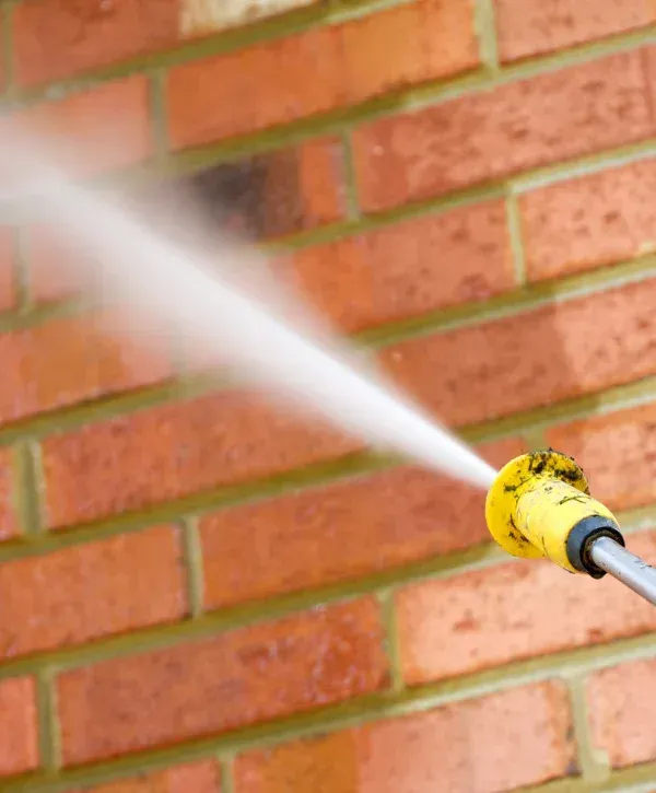 Pressure washer spraying water on brick wall exterior.