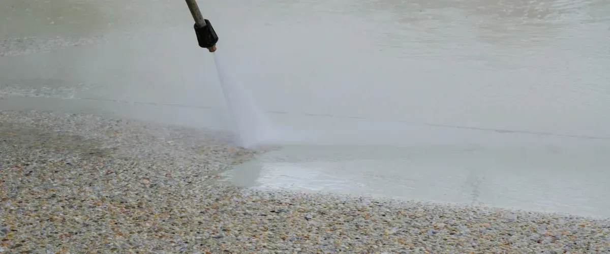 A power washing nozzle cleaning a dirty sidewalk, revealing the words 'POWER WASH' written in clean concrete.