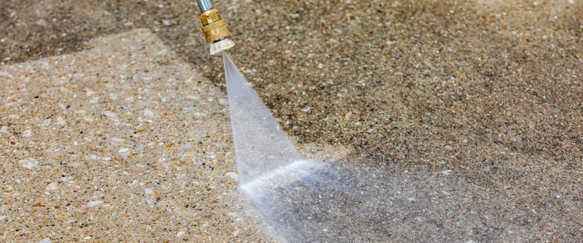 A close-up view of a pressure washer cleaning a concrete driveway, leaving a clean path behind it.