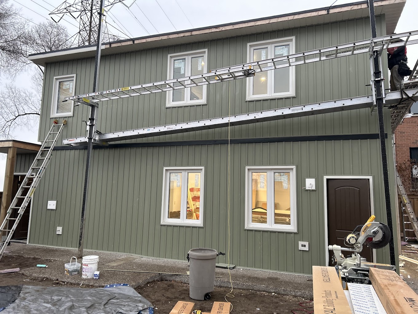 Two-story home exterior undergoing board and batten siding installation with scaffolding and equipment on-site.