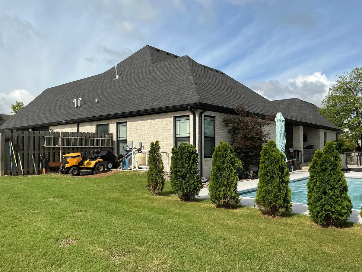 Brick home with new dark asphalt shingle roof by backyard pool
