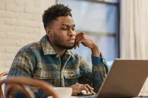 Black man in Plaid flannel shirt sitting in front of a laptop with a coffee cup