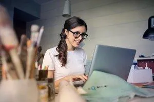 White woman with dark hair and dark eyeglass frames looking at her laptop.  