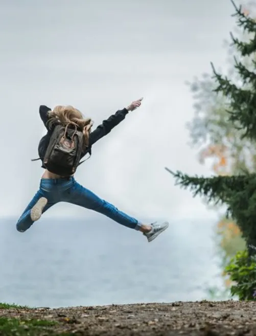 A young person wearing a backpack jumping in the air