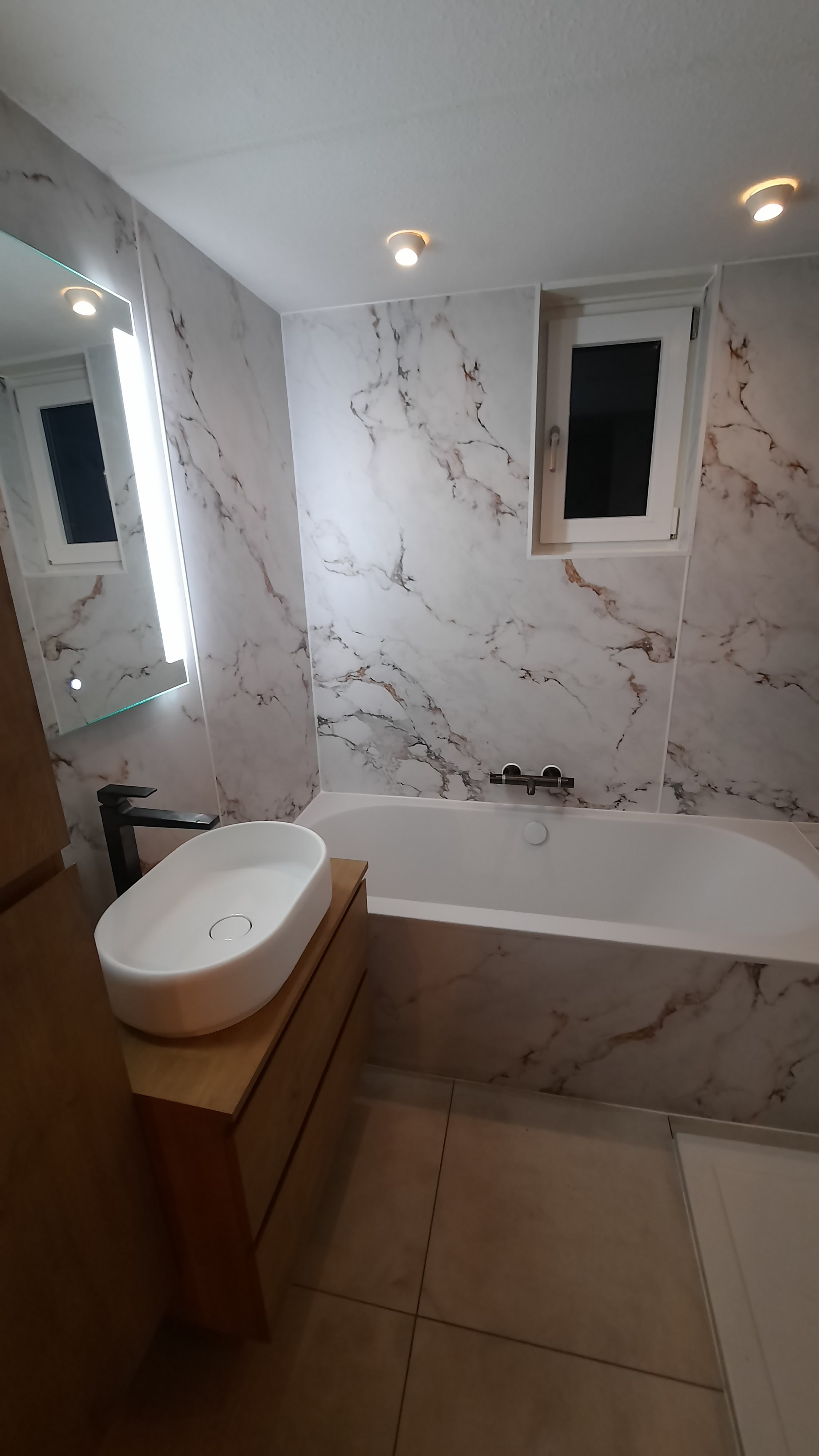 Luxe badkamerrenovatie in Renswoude door IMT Bouwservice met nieuw draaikiep-raam boven het bad en modern wastafelmeubel.