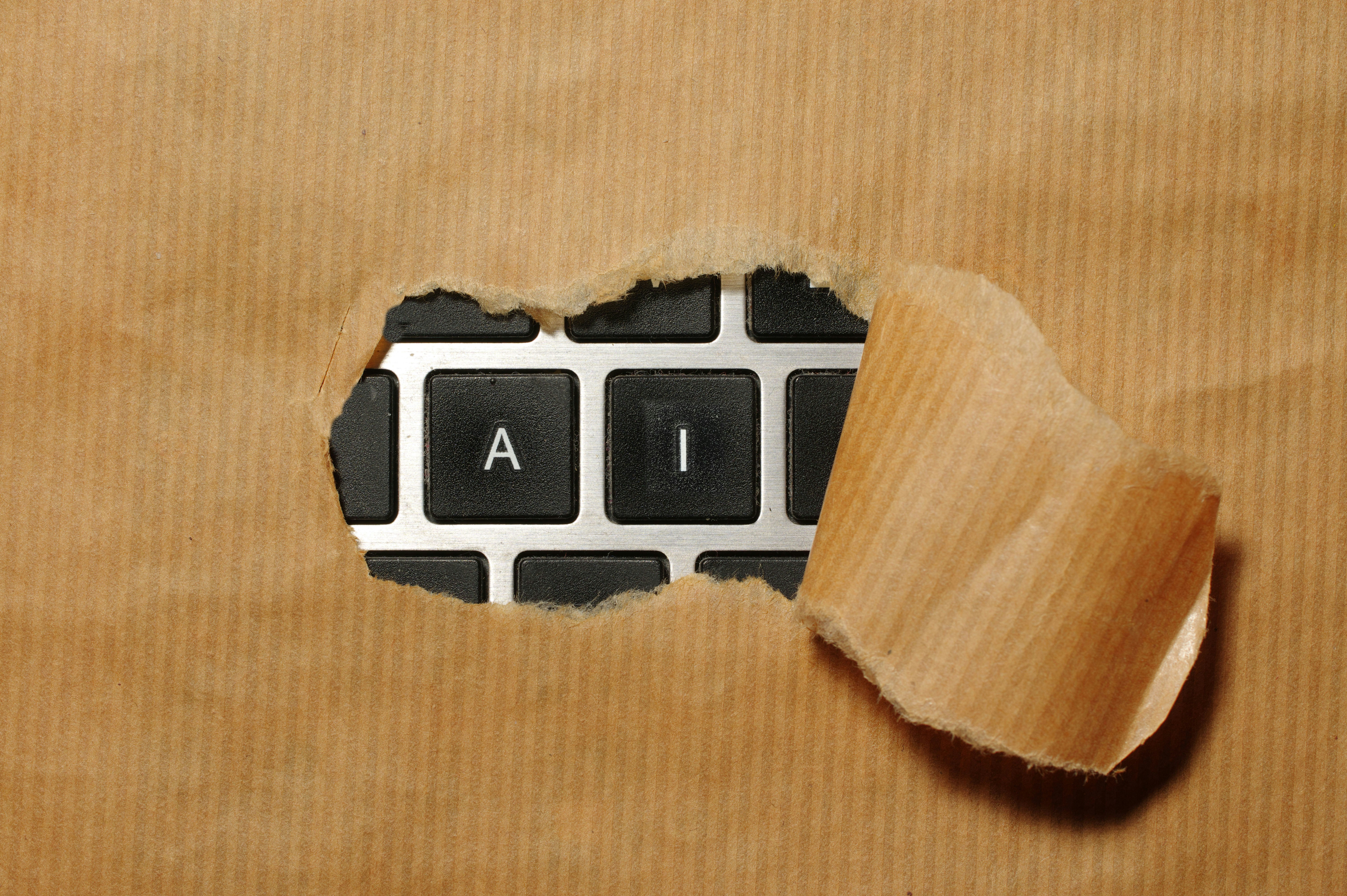 A piece of brown paper with a hole showing two keys from a keyboard that have the letters 'A' and 'I'.
