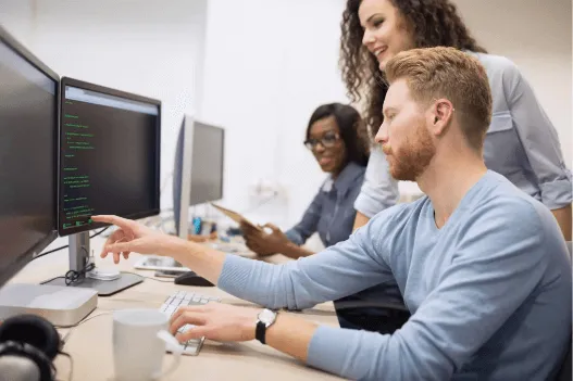 Team members discussing while pointing at a computer monitor during a meeting