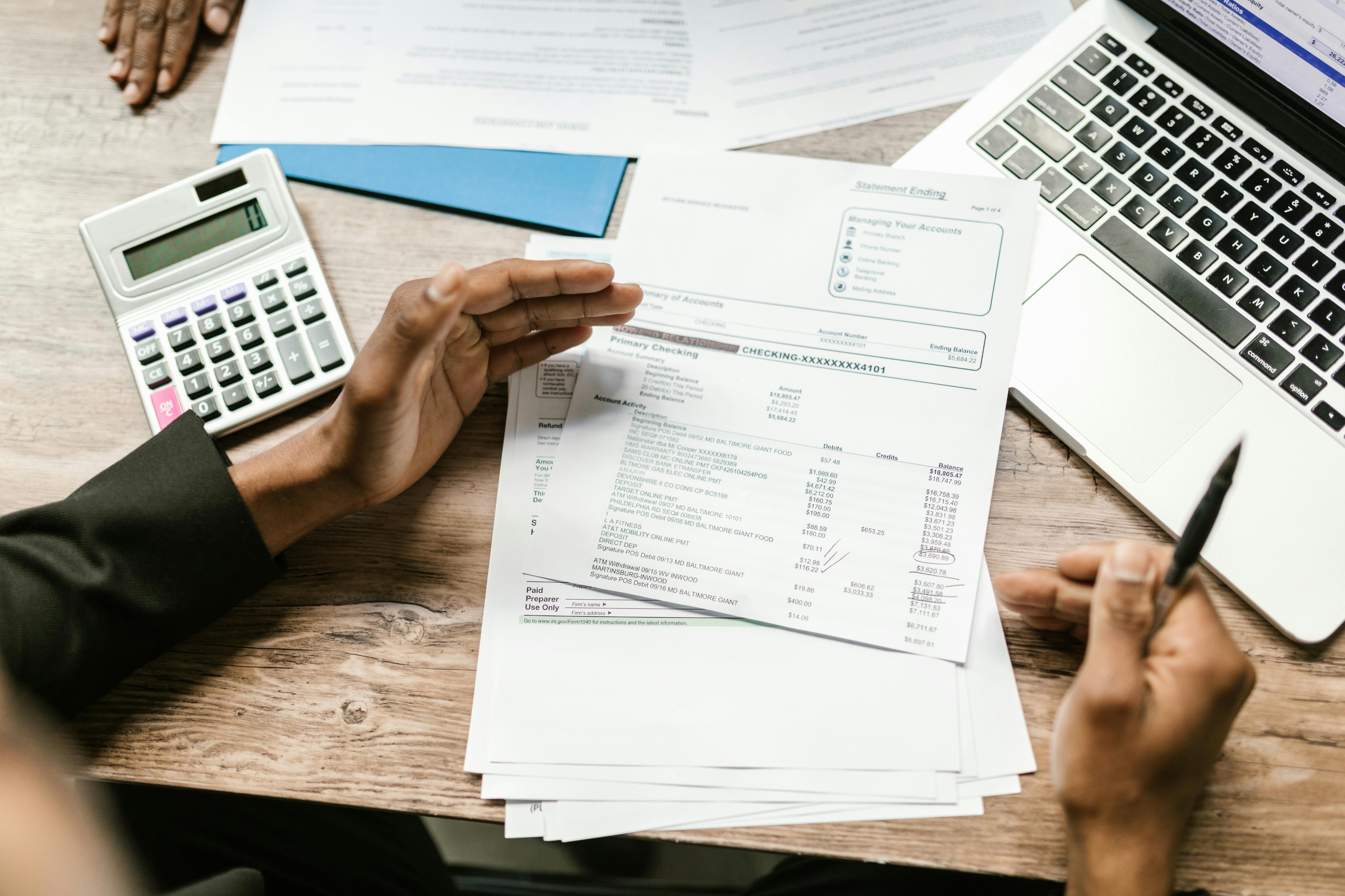 Hands holding financial documents with calculator and laptop on office desk, business analysis scene