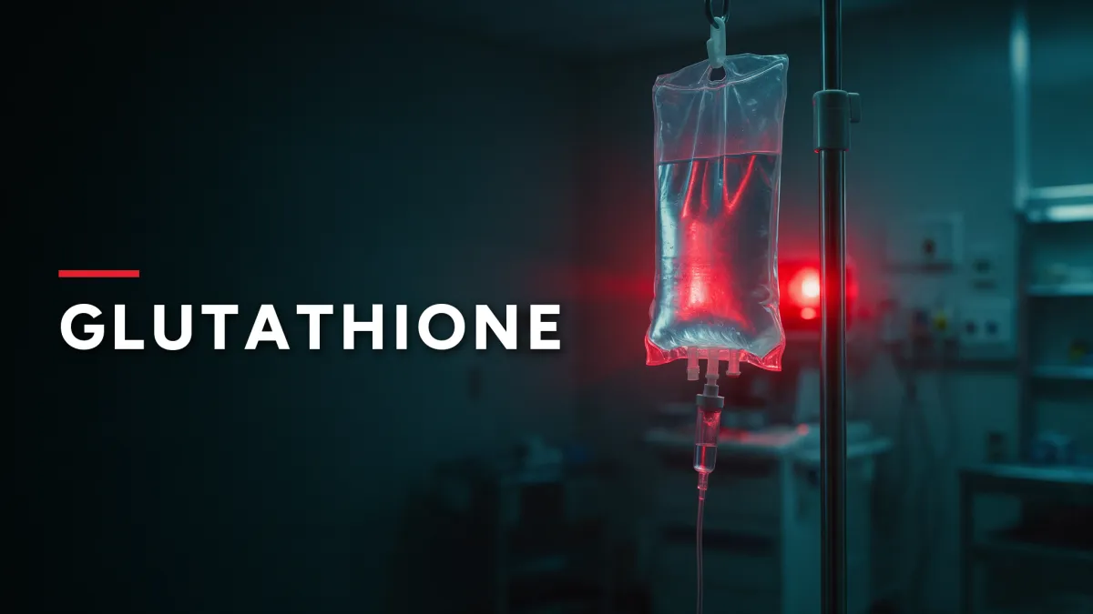 Clear IV bag hanging from an IV pole in a dark treatment room, lit by a red warning light, with the word "GLUTATHIONE" in white capital letters