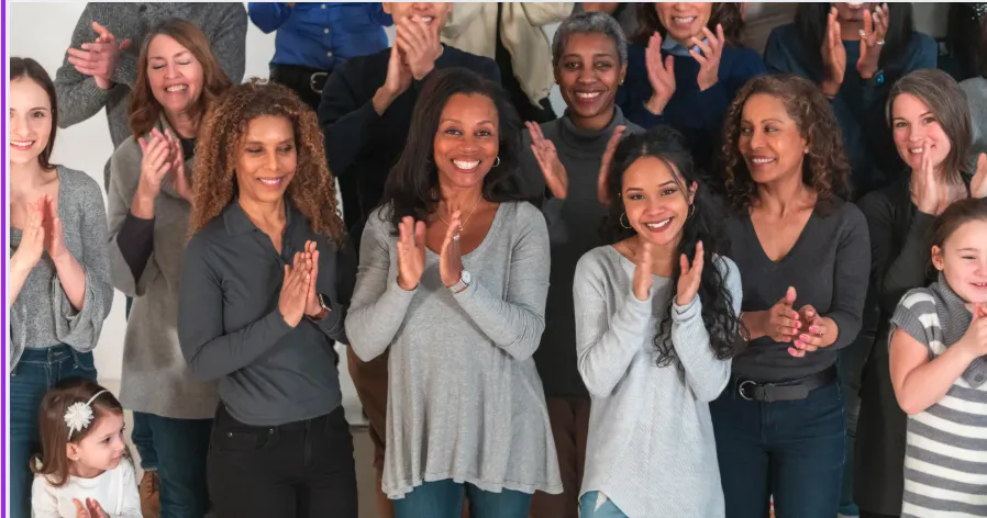 A diverse group of adults in a sunlit event space with peach and rose accents, smiling and engaging in conversation.