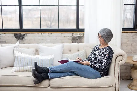 Woman relaxing on a sofa while reading and taking notes in a notebook.