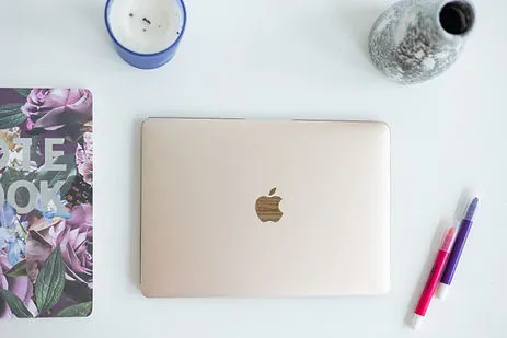 Closed laptop on a white desk with a notebook, coffee cup, vase, and colorful pens.
