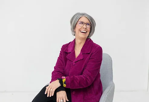 Smiling woman in a magenta jacket seated in a chair.