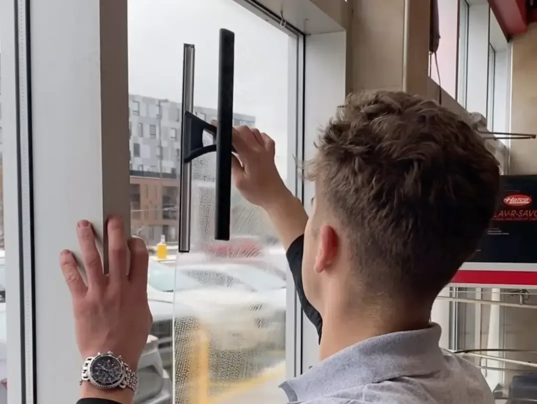Professional cleaner using a squeegee to wash interior windows of a commercial building.