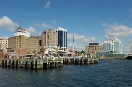 Sunny view of the Halifax waterfront boardwalk with people walking and the harbor in the background.