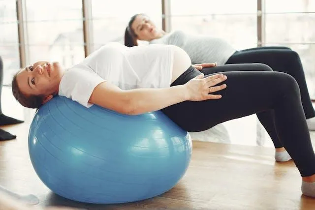 A pregnant woman using an exercise ball for exercise, focusing on maintaining fitness and comfort during her pregnancy.