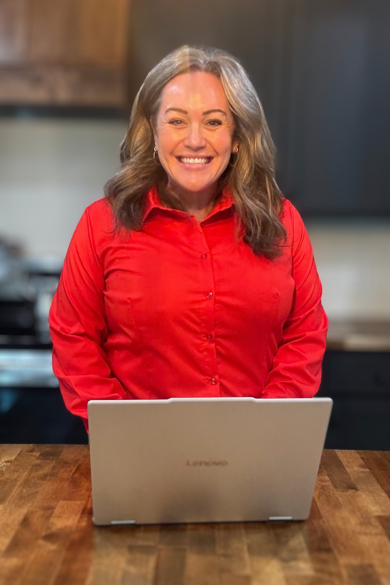 Carmen Ball smiling behind a laptop in a red top