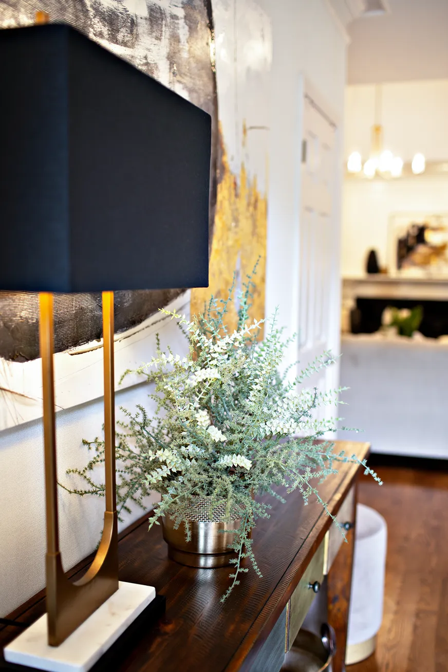 Wooden entryway console table withe a black and gold lamp and a rustic green plant in a gold planter.