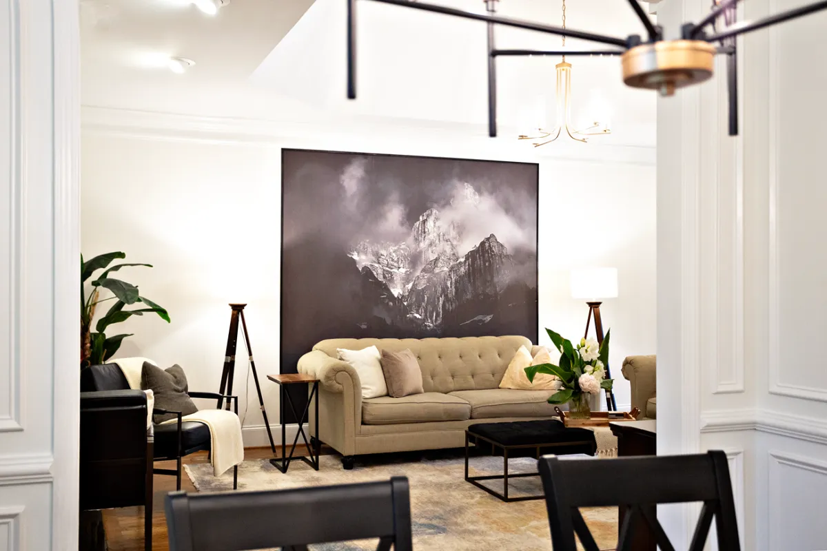 Traditional style living room showcasing a light brown linen sofa, black cushioned coffee table, and a dark floor to ceiling painting on white walls.