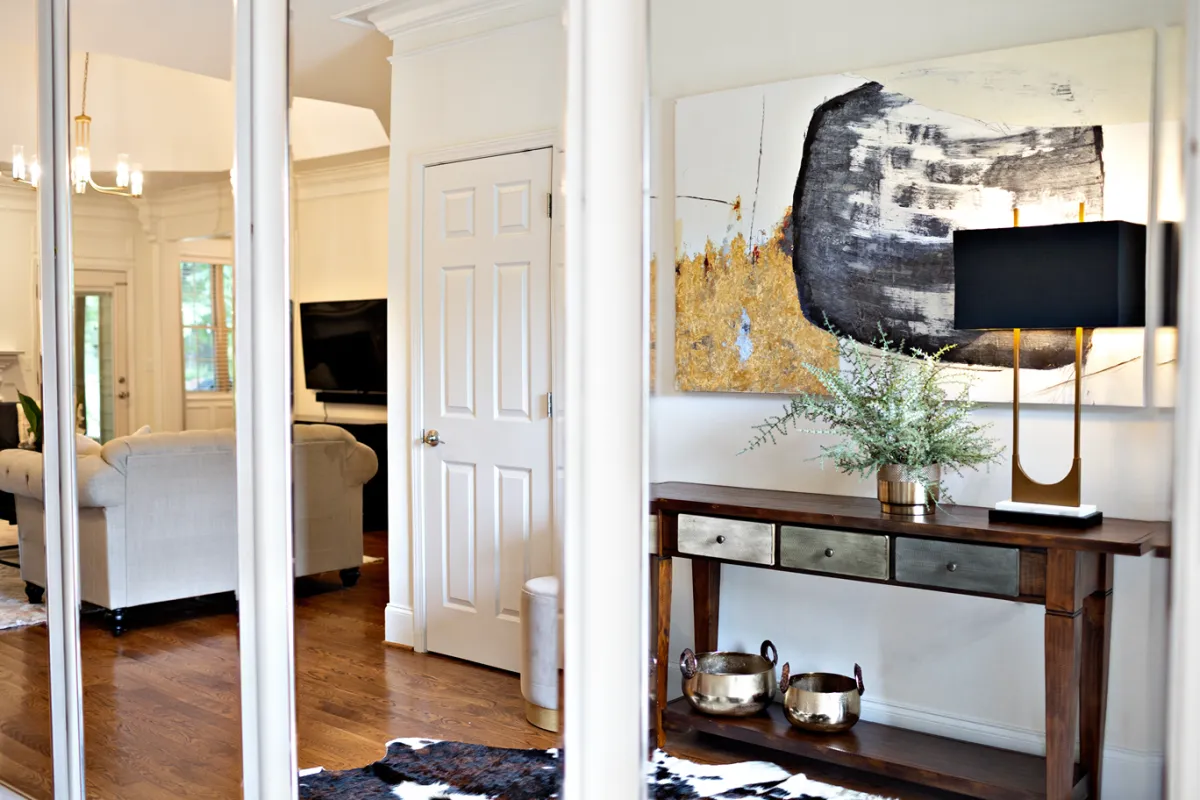 Rectangular mirror panels on an entryway wall showcasing the opposite wall which features dark wooden console table and gold and black abstract painting.  