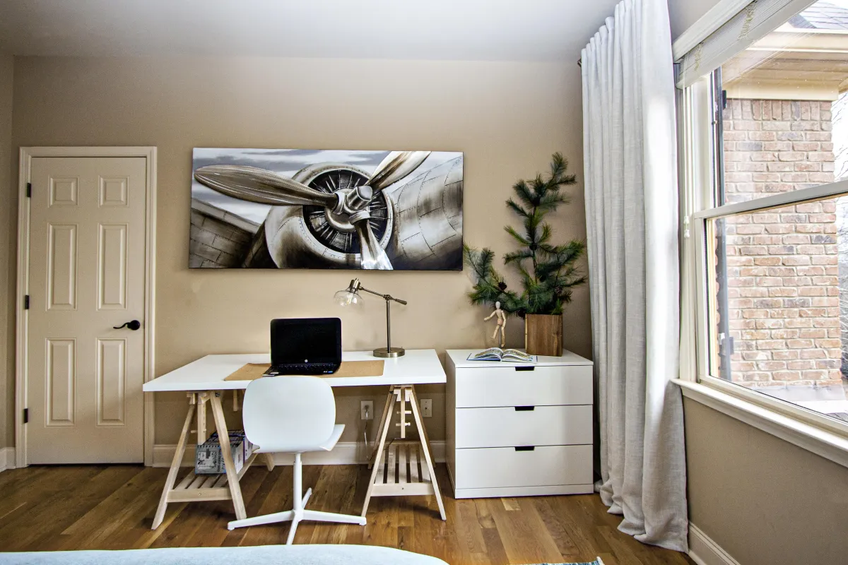 Cozy boys’ bedroom featuring a white desk and chair, white organizational cabinet, and wall art of a plane.